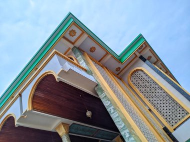 Bir caminin dış görünüşü, mimari detaylarını gözler önüne seriyor: kemerli kapı aralığı, dekoratif fayanslar ve bulutlu bir gökyüzüne karşı yeşil süsleme..