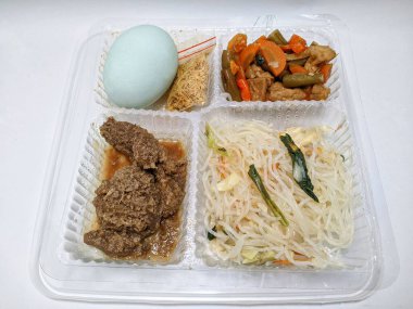 Temiz bir plastik kabın içinde düzgünce yerleştirilmiş et rendang, karıştırılmış sebze, pirinç vermicelli, tuzlanmış yumurta ve serundeng (kızarmış hindistan cevizi) içeren tabaklar..