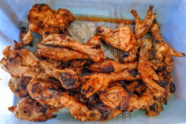 Genel bakış açısına göre, bir fotoğraf kaynamış, baharatlı ve sonra ızgara tavuk butları, kanatları, kafaları ve ayakları içeren altın ve siyah renkler içeren plastik bir kap yakalar..