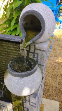 İki katmanlı taştan bir fıskiyenin yakından çekimi. Su üstten alta doğru incelikle çağlıyor. Kırsal dokusu ve huzurlu atmosferi ev dekorasyonu ve bahçe tasarımı temaları için ideal hale getiriyor..