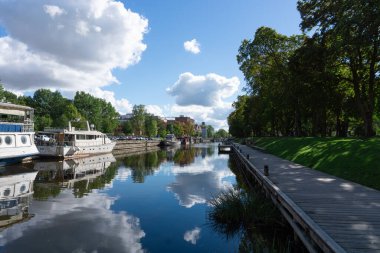 Tekneler, ağaçlar ve yansımalarıyla güzel bir yaz nehri kıyısı İsveç Uppsala