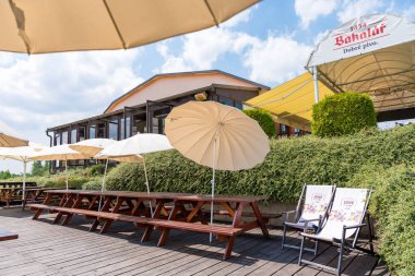 Prag, Çek Cumhuriyeti - 9 Haziran 2024: Terastaki Bobsleigh Kafe 'de dinlenmek ve yemek yemek için bir yer. Uzun ahşap piknik masaları, açık havada güneşli bir alanda gölgelik sağlayan beyaz şemsiyeler..