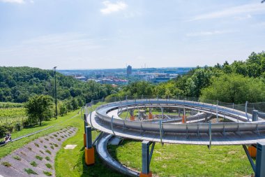 Prag, Çek Cumhuriyeti - 9 Haziran 2024: Prosek ilçesindeki Bobsleigh, yaz güneşinin aydınlattığı tepe ve yeşillik zeminine karşı şehrin manzarasını gösteriyor.