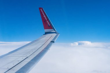 Prag, Çek Cumhuriyeti - 5 Temmuz 2024: Aşağıda beyaz bulutlar ve yukarıda açık mavi bir gökyüzü bulunan Norveç Havayolları uçağının kanadını gösteren bir uçak penceresinden çarpıcı bir manzara. 