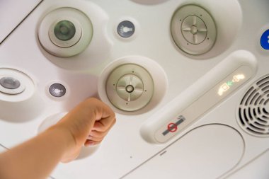 Havalandırma ve ışık düğmelerinin yer aldığı bir uçağın genel panelini ayarlamak için bir çocuğun eline yaklaş. Görüntü uçuş deneyimini ve yolcu rahatlığını yakalar..