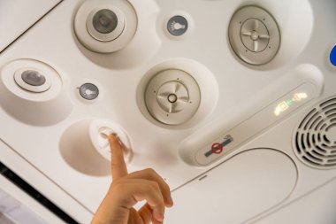 Havalandırma ve ışık düğmelerinin yer aldığı bir uçağın genel panelini ayarlamak için bir çocuğun eline yaklaş. Görüntü uçuş deneyimini ve yolcu rahatlığını yakalar..