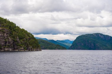 Norveç 'in Bergen kenti yakınlarında sakin sular ve bulutlu bir gökyüzü altında yemyeşil dağların yer aldığı fiyort manzarası. Yaz aylarında el değmemiş güzel bir duvar kağıdı..
