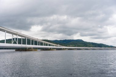 Norveç 'teki uzun Osteroy köprüsüne karşı yeşil tepeler ve gri gökyüzü, su seviyesi perspektifi