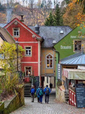 Schmilka, Almanya - 18 Kasım 2023: Sırt çantalı turistler, sonbahar atmosferinin tadını çıkararak şirin renkli evleri olan rahat sokaklar boyunca yürüyorlar.