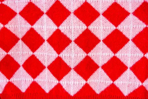 stock image A close-up of a vibrant red and white checkered knitted fabric, showcasing a classic argyle pattern. The textured material evokes a sense of warmth and comfort. Winter sweater or a blanket