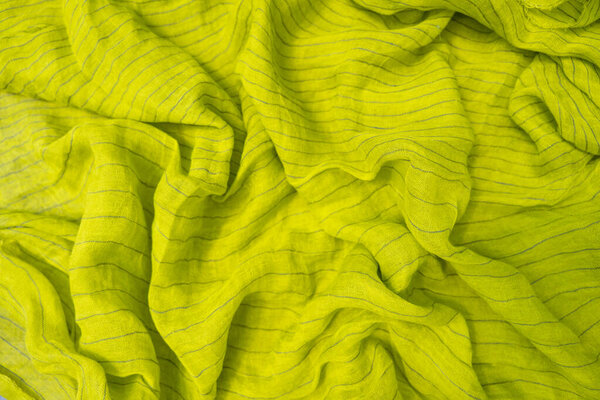 A vibrant lime green linen fabric with subtle stripes is draped in soft, natural folds. The close-up highlights the texture and rich color of the fabric, creating a lively, fresh atmosphere.