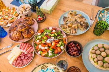 Ahşap bir masada ziyafetli bir Noel yemeğinin üst görüntüsü. Açık yüzlü sandviçler, taze salata, peynirli fırında et ve bir tabak sosis ve peynir dahil ev yapımı yemekler..