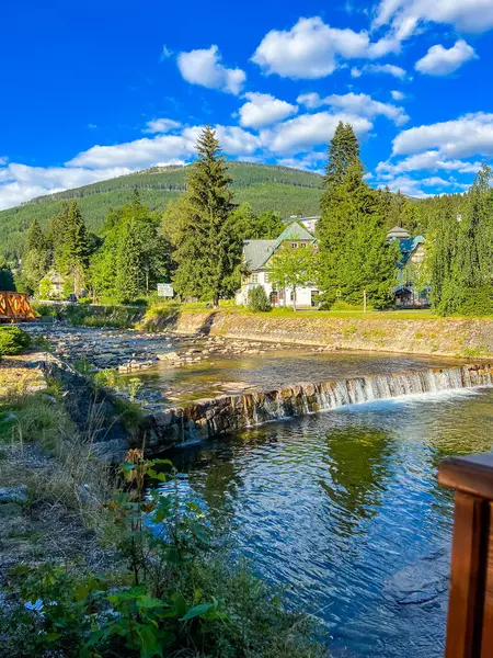 Çek Cumhuriyeti 'nin başkenti Spindleruv Mlyn' in ortasından, parlak bir yaz gününde huzurlu bir çağlayan nehir akar. Manzarada, sakin bir kentsel denge sunan uzak bir dağ yer alıyor..