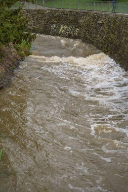 Prague, Czech Republic - September 16, 2024: A picturesque scene featuring the small river Rokytka in Palmovka district. The rushing waters reflect the threat of impending floods on a cloudy day. clipart