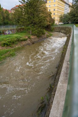Prag, Çek Cumhuriyeti - 16 Eylül 2024: Palmovka bölgesindeki Rokytka nehrinin küçük bir sahnesi. Akan sular, bulutlu bir günde yaklaşan sel tehdidini yansıtıyor..