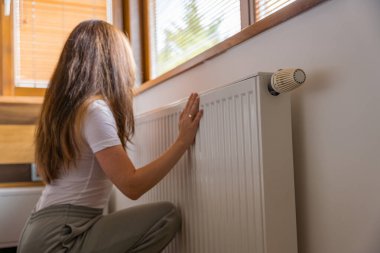 Isınma mevsimi başlarken bir kadın sıcak bir evde radyatörü ayarlar. Pencereden süzülen güneş ışığı sahneye sıcaklık katar ve serin günlerin başladığını gösterir..