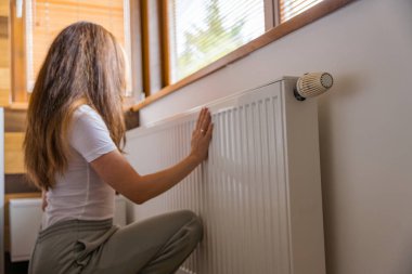 Isınma mevsimi başlarken bir kadın sıcak bir evde radyatörü ayarlar. Pencereden süzülen güneş ışığı sahneye sıcaklık katar ve serin günlerin başladığını gösterir..