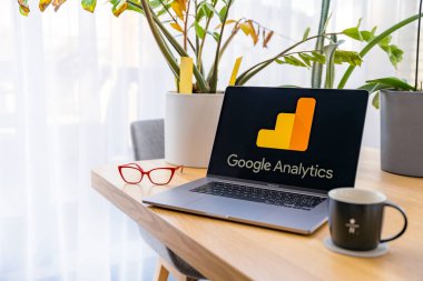 Prag, Çek Cumhuriyeti - 20 Eylül 2024: Google Analitik logosunu ekranında gösteren bir laptop MacBook Pro bir çift kırmızı bardak ve bir kahve bardağının yanındaki ahşap masada oturuyor.