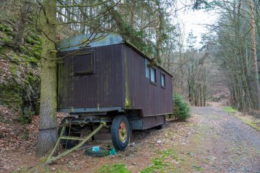 Çek Cumhuriyeti 'nin sessiz bir ormanında terk edilmiş, paslı, ahşap bir karavan duruyor. Yosun ve kir yapıyı kaplıyor, çürümeyi vurguluyor. Sahne izolasyon ve unutulmuş zamanı çağrıştırıyor..
