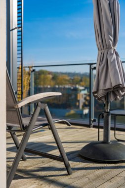 Prag 'da bir teras açık bir sonbahar gününde katlanmış gri bir şemsiye ve metal bir sandalyeyle. Parlak mavi gökyüzü mobilyaların sessiz tonlarıyla çelişiyor. Kimse yok..