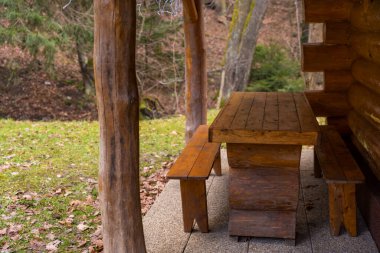 Rustic wooden table with two benches near a log cabin on a cloudy winter snowless day in a Czech forest. Cottage core, copy space, no people. clipart