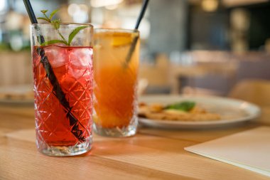 İki mocktail, nar şurubu ve kırmızı limonatalı Cinderella, yumuşak odaklı ahşap bir masada. Sıcak tonlar, yakın çekim görüntüsü ve sığ alan derinliği kopya alanı ile samimi bir ortam oluşturur