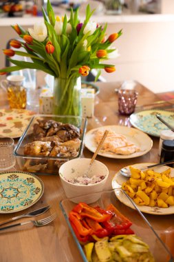 Çok güzel bir yemek masası. Ortası ev yapımı yemekler, kızarmış tavuk, somon, ızgara sebze ve patatesle çevrili canlı bir lale buketiyle. Davetkar atmosfer