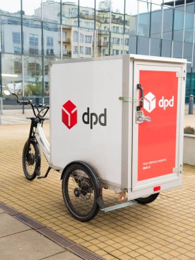 Prag, Çek Cumhuriyeti - 8 Ocak 2025: Asfaltlı bir alana park edilmiş DPD logosu olan elektrikli kargo üç tekerlekli bisiklet. Modern şehir manzarası arka plandaki cam bir binaya yansıyor.. 