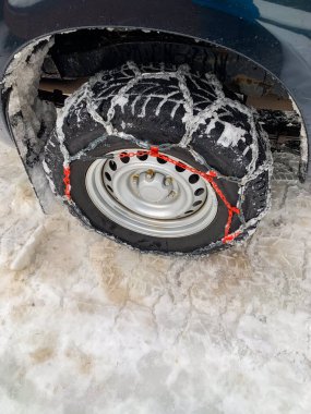 Buzlu yollarda daha iyi yol tutuşu için metal kar zincirleriyle donatılmış bir araba tekerleğinin yakın çekimi. Lastik kar ve buzla kaplı ve kış koşullarını vurguluyor. Ayrıntılar için hafif bir açıyla çekilmiş.