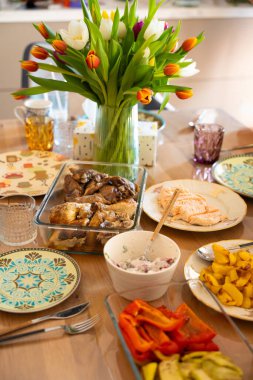 Çok güzel bir yemek masası. Ortası ev yapımı yemekler, kızarmış tavuk, somon, ızgara sebze ve patatesle çevrili canlı bir lale buketiyle. Davetkar atmosfer.