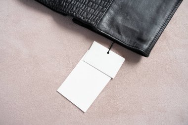 Beyaz etiketli, bej desenli bir arka plana yerleştirilmiş siyah deri korse kemerinin yakın çekimi. Minimalist kompozisyon dokuyu vurgular, aksesuar ayrıntıları.