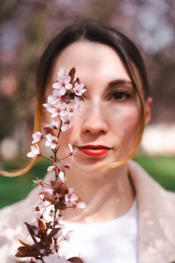 Prag, Troja Garden 'da bej ceketli beyaz kadın kiraz çiçekleri tutuyor. Yumuşak odak ve sıcak tonlar, ilkbahar estetiği ve doğal güzelliğiyle rüya gibi, sanatsal bir portre oluşturur..