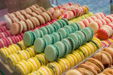 Canlı Fransız Makaronları 'nın yakın çekim görüntüleri bir pastanede sırayla dizilmiş. Sarı, yeşil, kırmızı ve kahverenginin parlak renkleri görsel olarak çekici bir tatlı seçimi oluşturur..