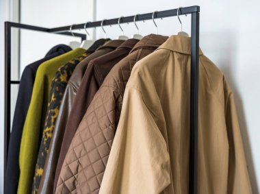 Sonbahar, kış ve bahar mevsimlerinin yakın plan çekimleri. Parlak bir elbise rafında asılı duran toprak renkler. Seçimde yün, deri ve yorgan ceketler yer alıyor. Kapalı alanda, gün ışığında yakalandılar. 