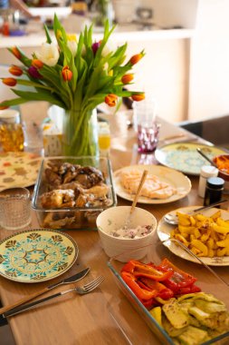 Çok güzel bir yemek masası. Ortası ev yapımı yemekler, kızarmış tavuk, somon, ızgara sebze ve patatesle çevrili canlı bir lale buketiyle. Davetkar atmosfer