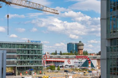 Prag, Çek Cumhuriyeti - 28 Temmuz 2024: Modern ofis binaları, bir inşaat vinci ve tarihi su kulesinin yer aldığı bir şehir manzarası. Bauhaus mağazası ve Novartis ofisi.