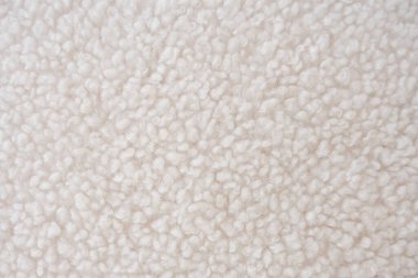 Dalgalı, kıvırcık desenli, pelüş, beyaz şerpa postu kumaşının detaylı yakın çekimi. Geri dönüştürülmüş polyesterden yapılan bu sürdürülebilir malzeme genellikle kışlık giysilerde, battaniyelerde ve iç kısımlarda kullanılır..