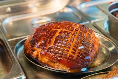 Mükemmel çizilmiş ve karamelize edilmiş derisi olan, paslanmaz çelikten bir tepside servis edilen, altın sarısı kahverengi bir jambonun yakın çekimi. Camlar çıtır çıtır dokuları ön plana çıkarıyor, görsel olarak çekici bir gurme yemeği..