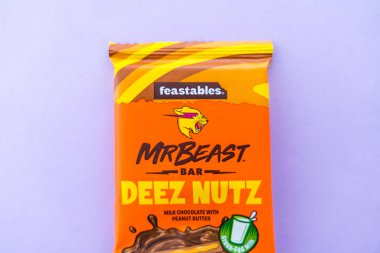 Prague, Czech republic - January 24, 2025: Close-up of MrBeast Feastables Deez Nutz chocolate bar on a pastel purple background. The bright orange packaging features bold branding and peanut butter. clipart