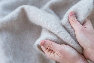 Beyaz beyaz yün kumaşı nazikçe tutan beyaz beyaz ellerin yakın çekimi, sıcaklığı, lüksü ve dokuyu vurguluyor. Yumuşak lifler ve nötr renk yumuşaklığı ve yüksek kaliteyi vurgular.
