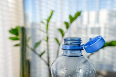 Close-up of a transparent PET bottle with a blue attached cap, designed for easy recycling. Captured in soft daylight, blurred background, eco-friendly packaging solutions, sustainability efforts. clipart