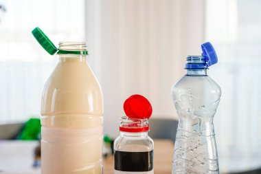 Close-up of three PET bottles with stationary plastic caps in green, red, and blue. The eco-friendly design keeps caps attached for easier recycling. Neutral background, sustainability concept. clipart