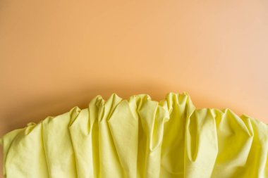 Yumuşak pastel arka planda toplanmış sarı bir kumaşın yakın çekimi. Katlar dokulu ve dinamik bir kompozisyon oluşturuyor. Kopya alanı ile modern estetik, moda ayrıntıları ve tekstil tasarım kavramı.