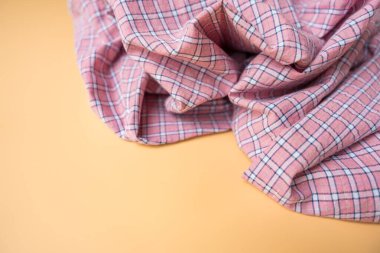 Kayısı arka planında yumuşak kıvrımlı pembe bir ekose kumaş. Damalı desen beyaz, donanma ve yeşil çizgilerden oluşuyor. Tekstil dokusu görünür, sıcak estetik..
