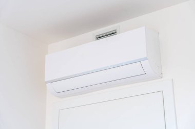 Modern bir evin içinde, beyaz bir duvarın üzerine monte edilmiş beyaz bir klima ünitesinin yakın çekimi. Enerji verimliliği ve konfor için minimalist iklim kontrol teknolojisi. İnsan yok, kopyalama alanı.