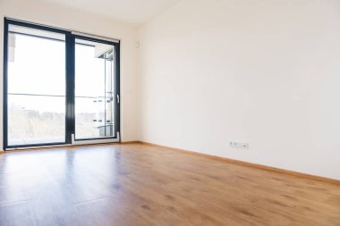 Modern bir dairede parlak boş bir oda. Eğimli ve dönüşlü pencere sistemi, ahşap döşeme ve minimalist bir tasarımı var. Büyük pencereler doğal ışık ve şehir manzarası sağlar. İnsan yok, kopyalama alanı