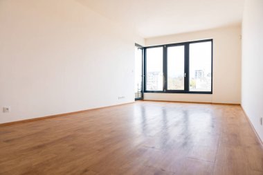 Modern bir dairede parlak, boş bir oda, eğimli ve pencereli, ahşap döşemeli, ve geniş bir iç döşemeli. Büyük pencereler doğal ışık ve şehir manzarası sağlar. Gayrimenkul için ideal