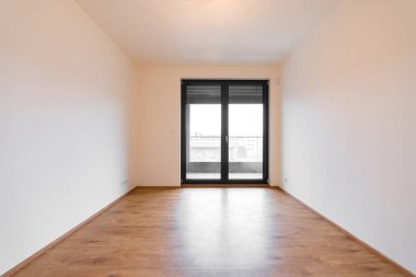 Modern bir dairede parlak boş bir oda. Eğimli ve dönüşlü pencere sistemi, ahşap döşeme ve minimalist bir tasarımı var. Büyük pencereler doğal ışık ve şehir manzarası sağlar. Kimse yok.