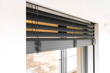 Modern bir apartmanın balkonunda, pencereleri ve kapıları kapalı paten panjurlarıyla yakın çekim yapın. Koyu gri alüminyum çerçeve, ışığın iç kısmıyla tezat oluşturuyor. Kimse yok..