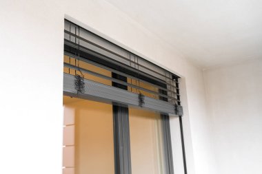 Modern bir apartmanın balkonunda, pencereleri ve kapıları kapalı paten panjurlarıyla yakın çekim yapın. Koyu gri alüminyum çerçeve, ışığın iç kısmıyla tezat oluşturuyor. İnsan yok, kopyalama alanı